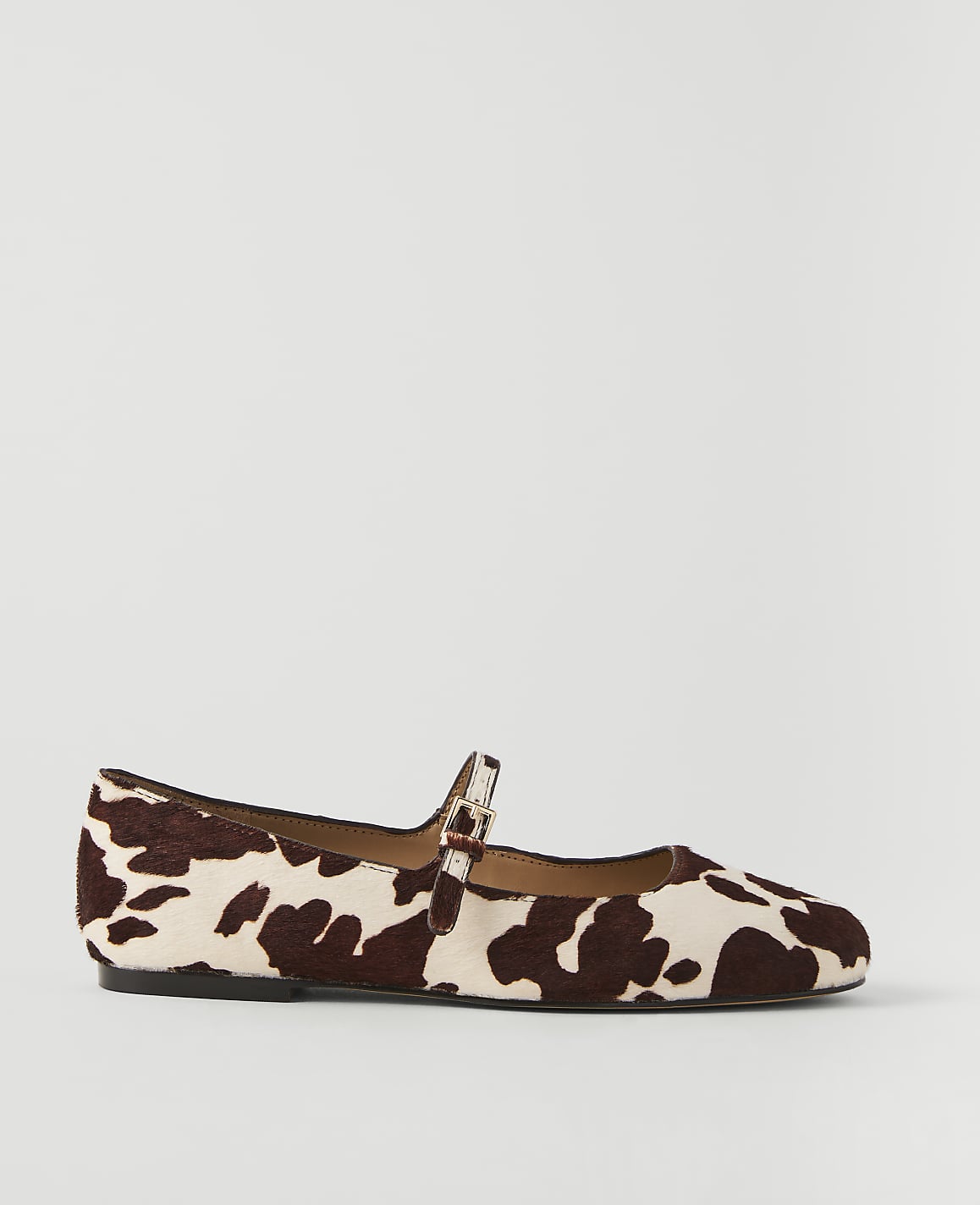 A cow-print Mary Jane flat shoe rests on a plain white background.