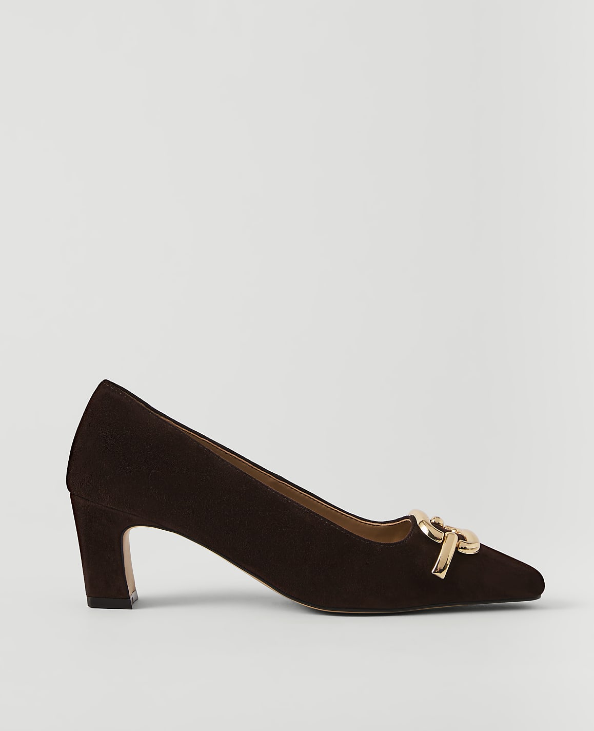 A dark brown suede pump with a gold buckle detail rests on a plain white background.