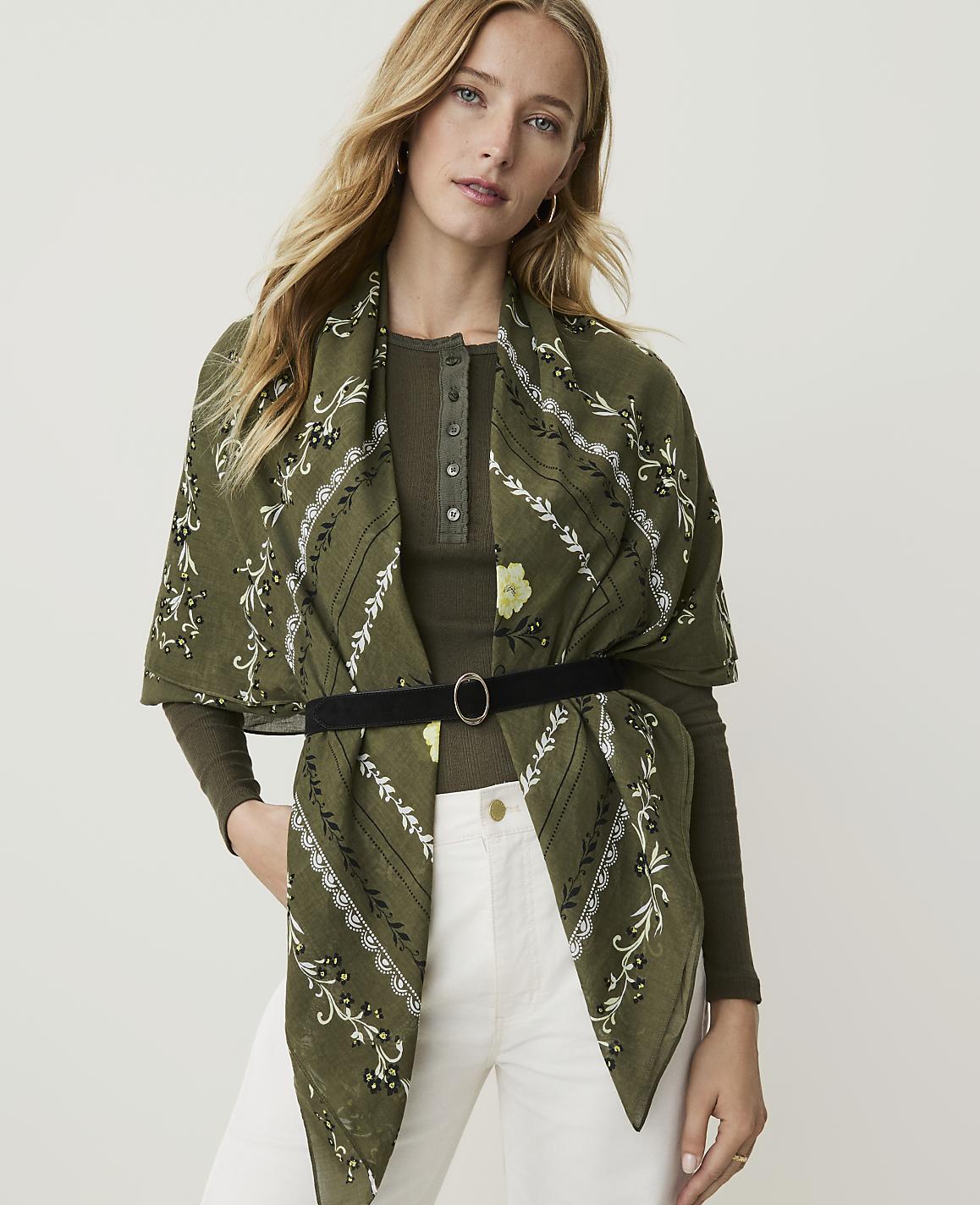 A draped olive green scarf with a white floral pattern lies on a plain white background.