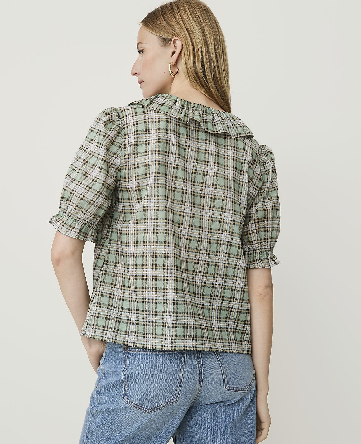 A woman in a plaid blouse and jeans stands against a plain white background.