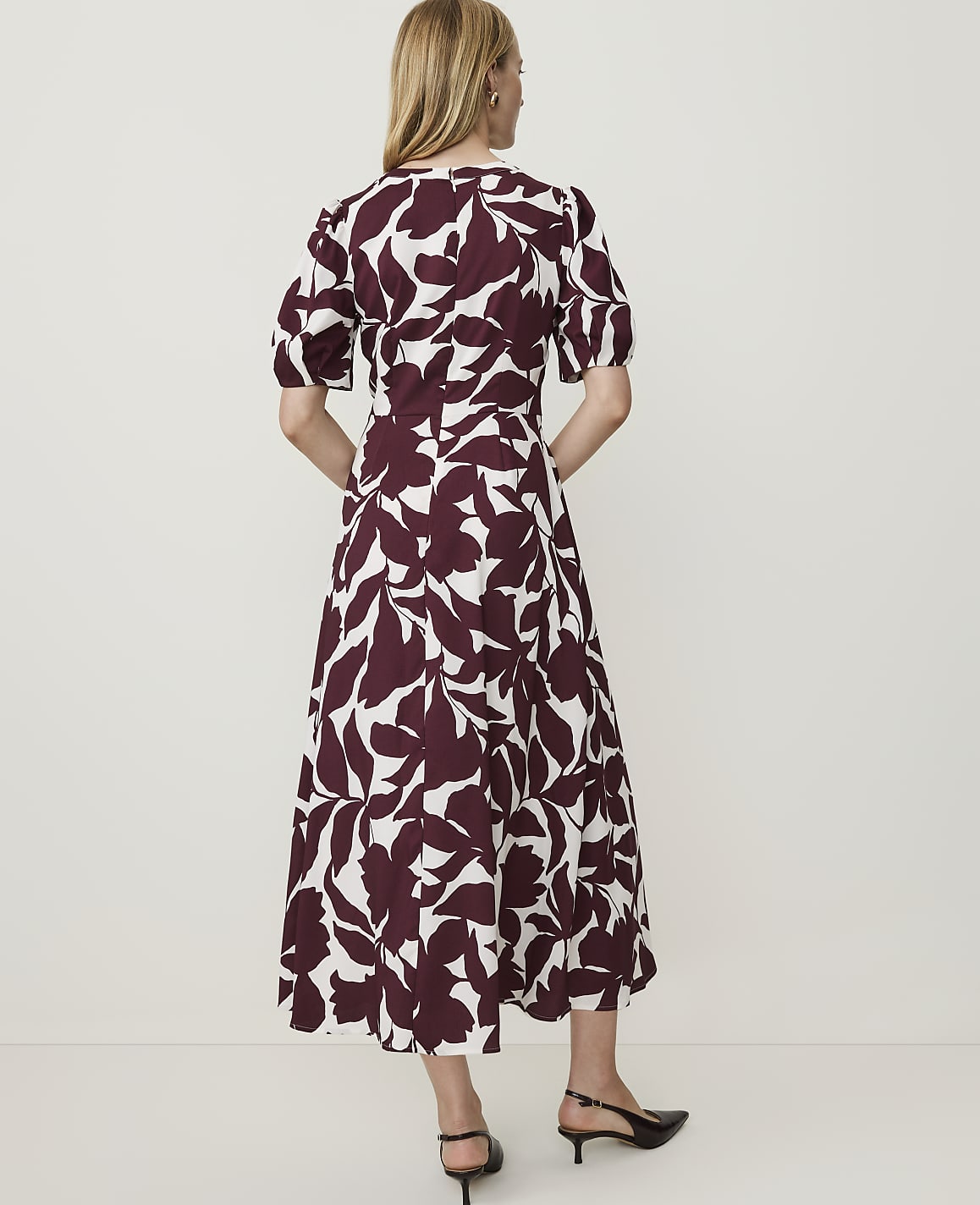 A woman in a white and burgundy floral dress stands against a plain white background.