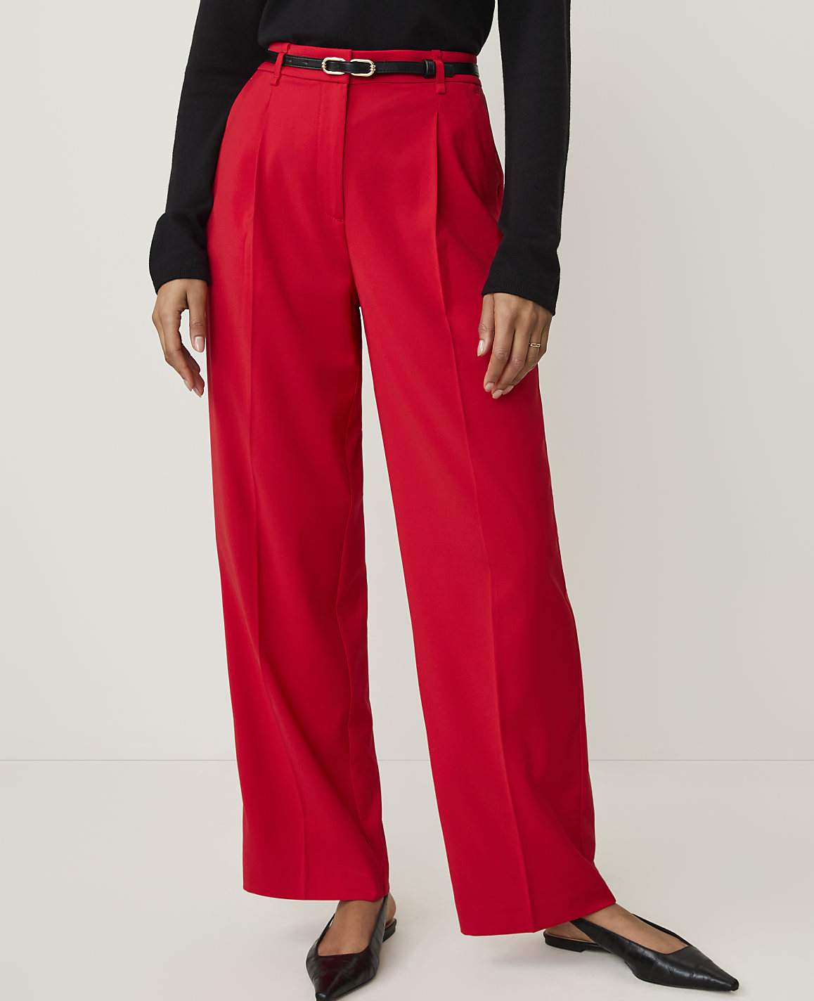 A person wearing bright red wide-leg trousers and black pointed-toe flats stands against a plain white background.