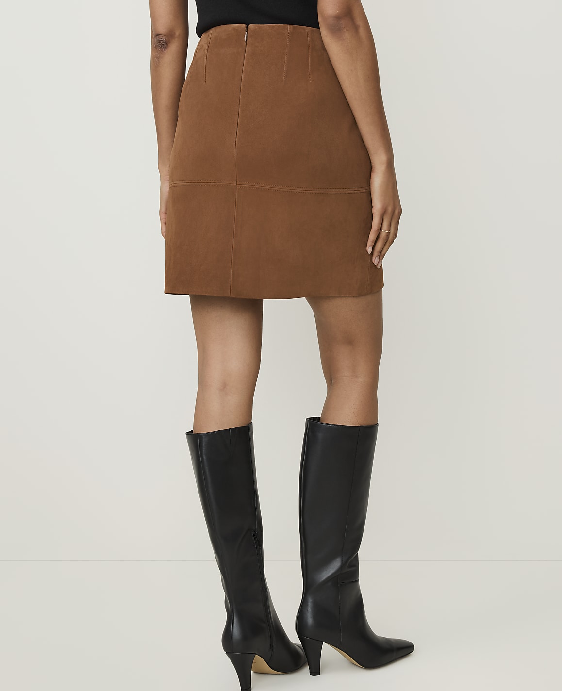 A person wearing a brown corduroy skirt and black knee-high boots stands against a plain white background.