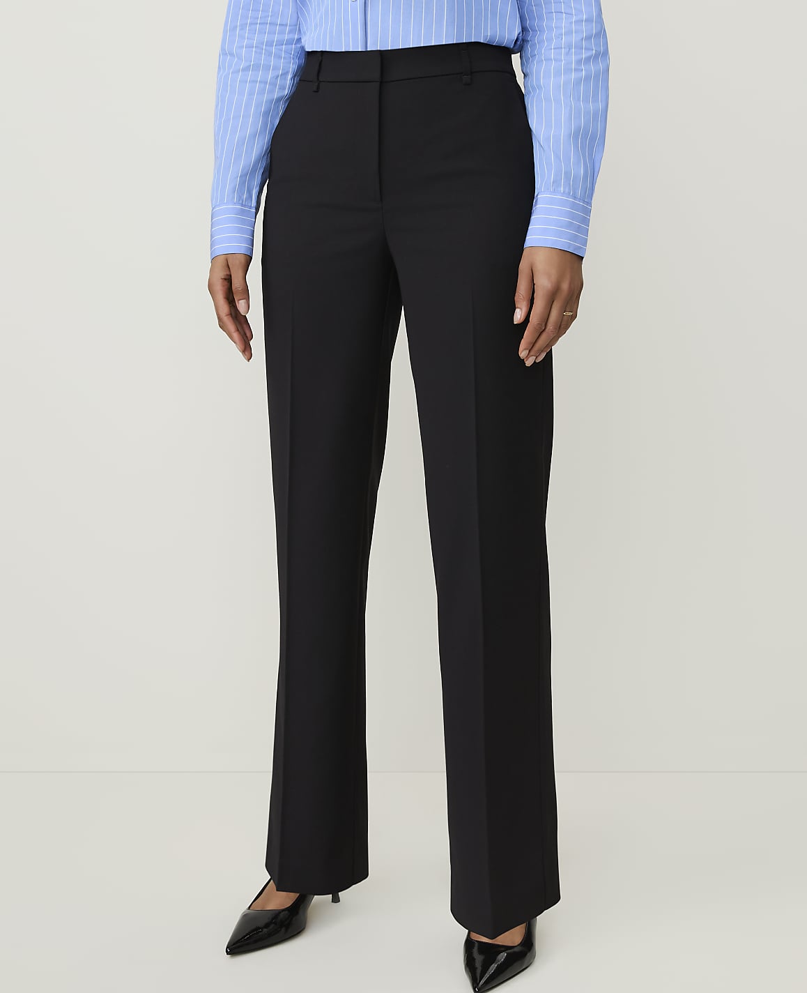 A person stands in black dress pants and a blue striped shirt against a plain white background.