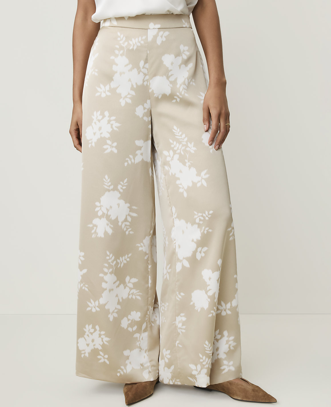 A person stands wearing wide-leg beige pants with a white floral pattern, against a plain white background.