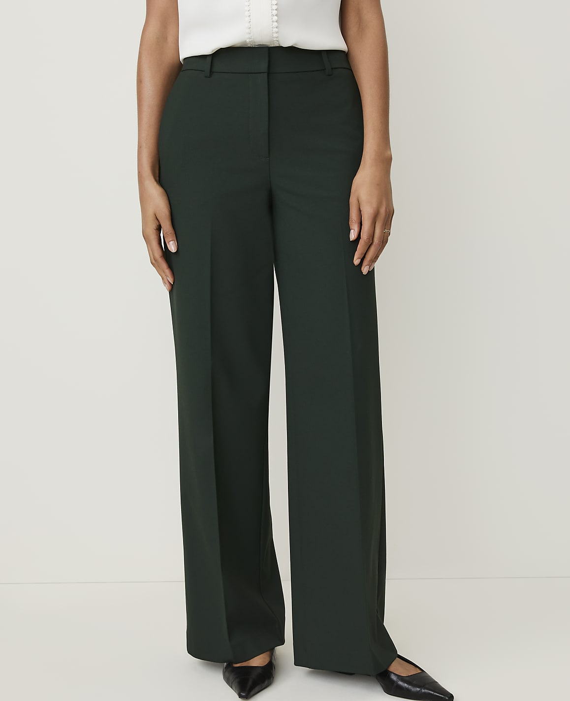 A person stands in dark green wide-leg pants and black pointed-toe flats against a plain white background.
