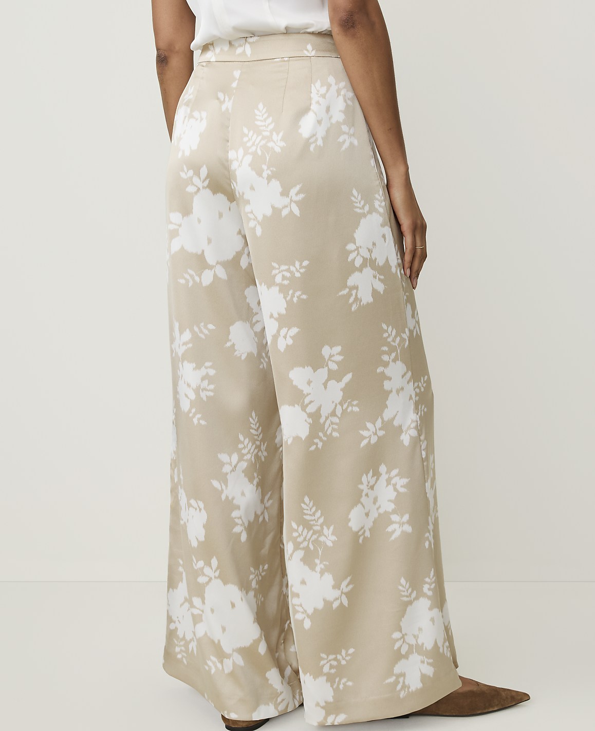 A person wears wide-leg, floral-patterned pants against a plain, light-colored background.