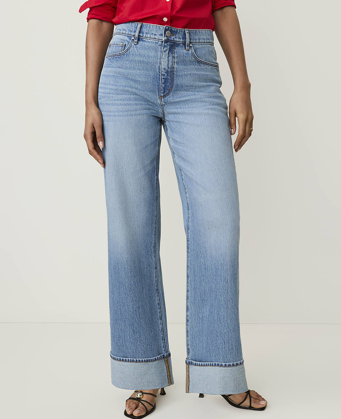 A person stands in light-wash, wide-leg jeans with cuffed hems and a red top against a plain white background.