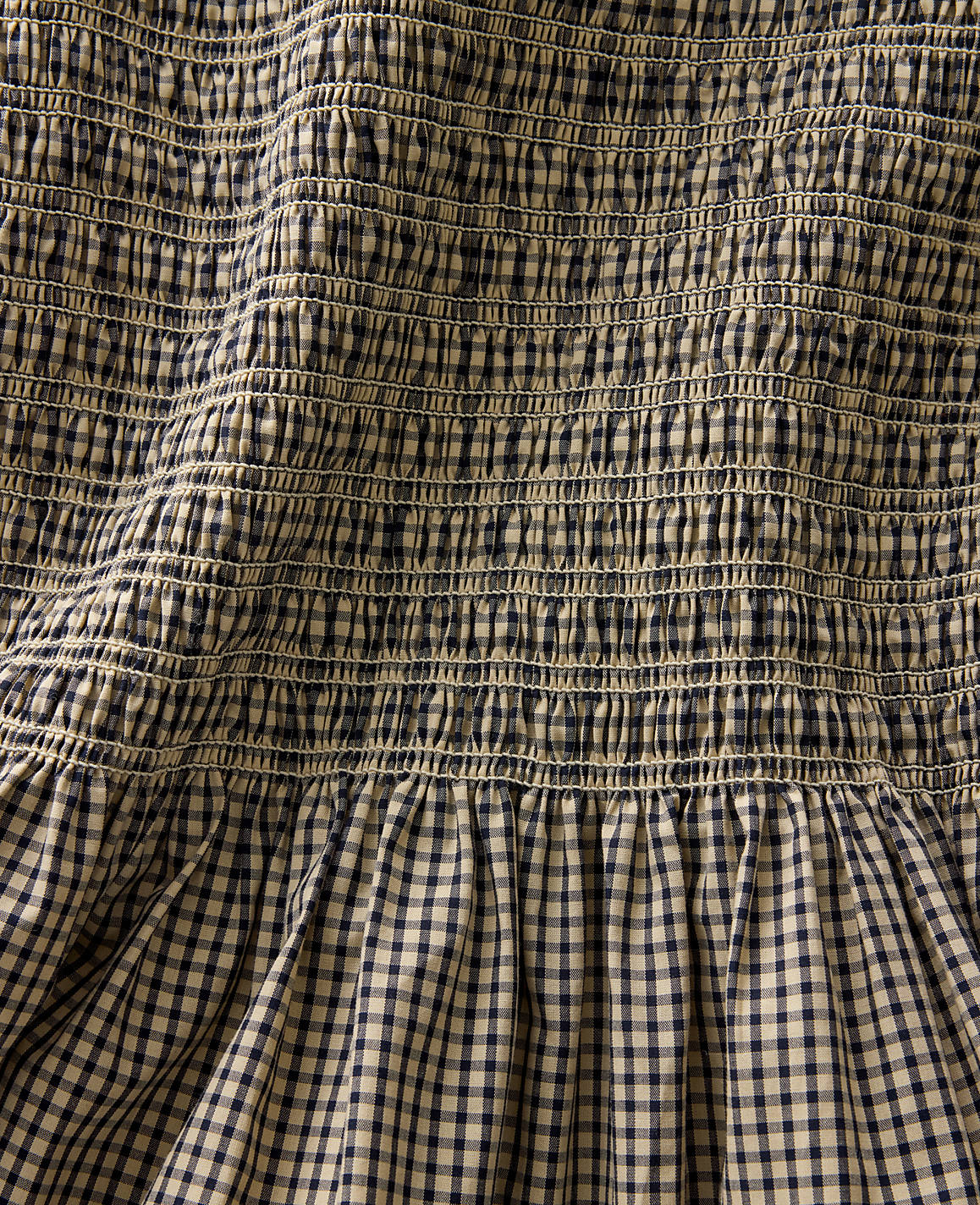 A close-up view of smocked fabric in the foreground transitions to a gathered gingham pattern in the background.