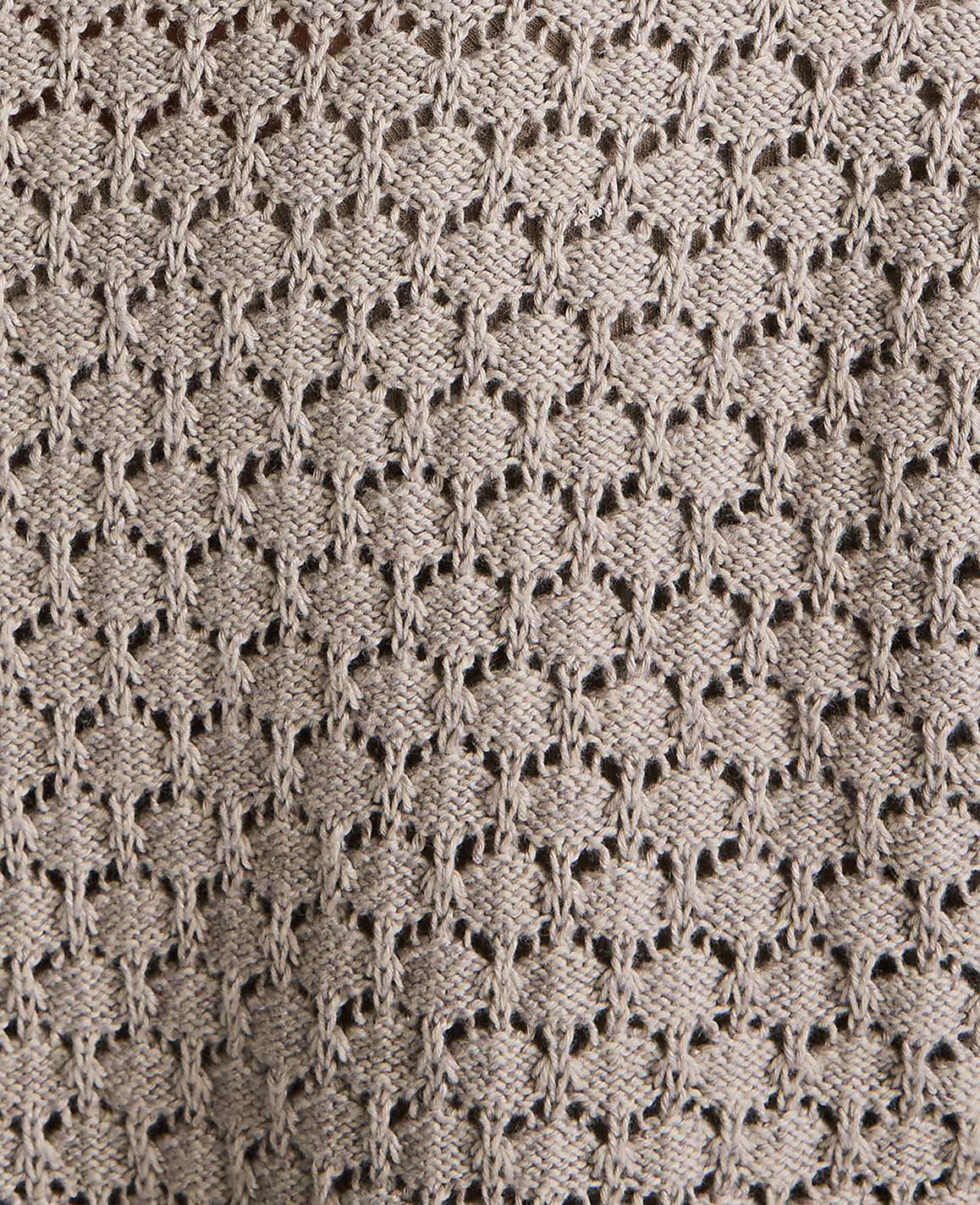 A close-up view of a beige knitted fabric with a repeating diamond-shaped lace pattern fills the frame.