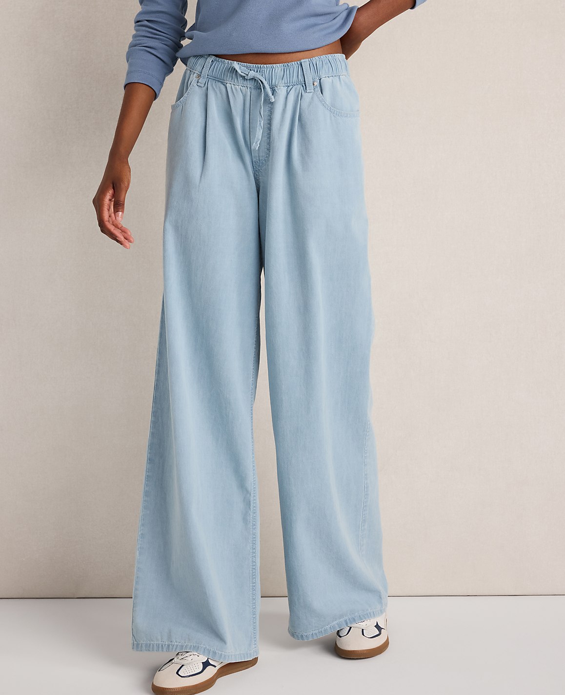 A person stands in light blue wide-leg jeans and sneakers against a plain white background.