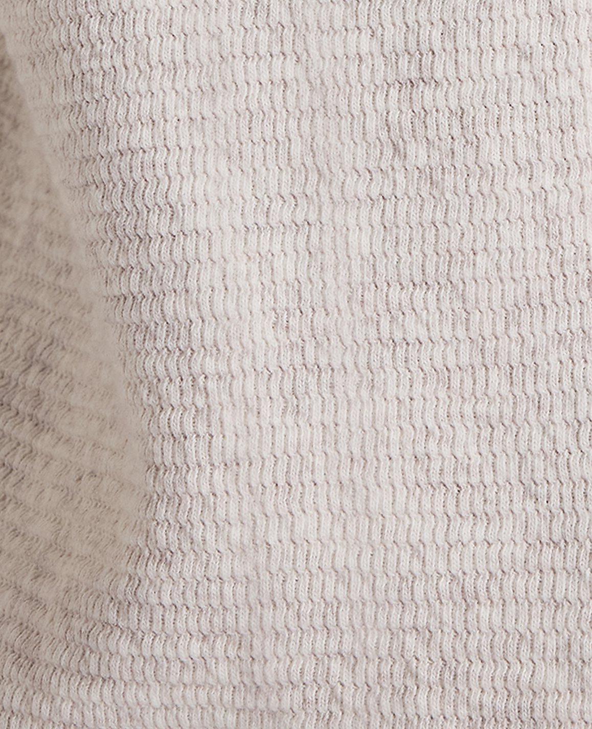 A close-up view of a textured, light gray fabric fills the frame, with subtle variations in shade creating a soft, mottled background.