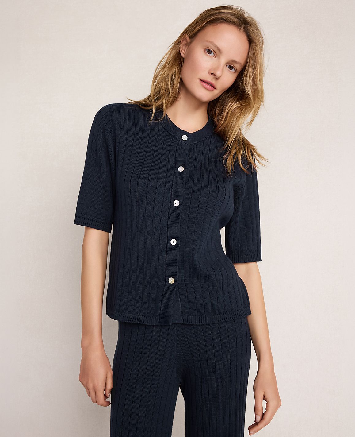 A woman in a navy ribbed cardigan and matching pants stands against a plain, light-colored background.