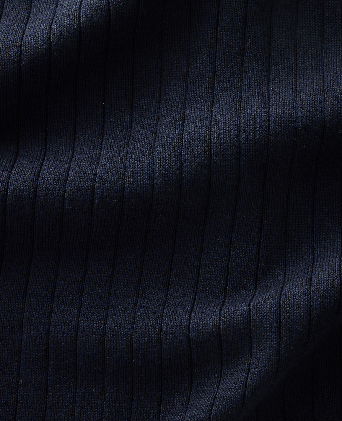 A close-up view of dark navy ribbed fabric fills the frame, with subtle shadows highlighting the vertical texture.