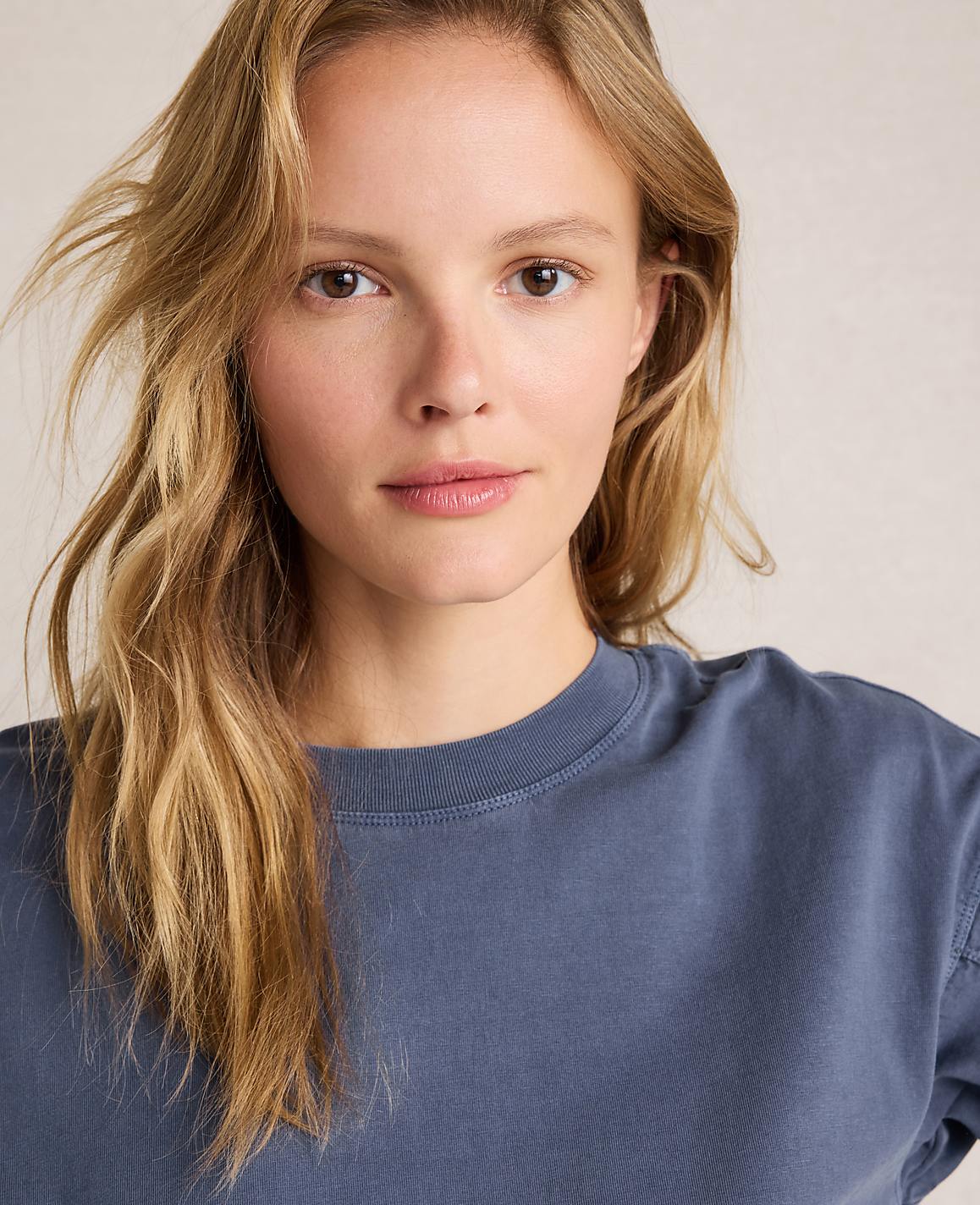 A young woman with blonde hair and a blue shirt is in the foreground, with a plain, light-colored background.