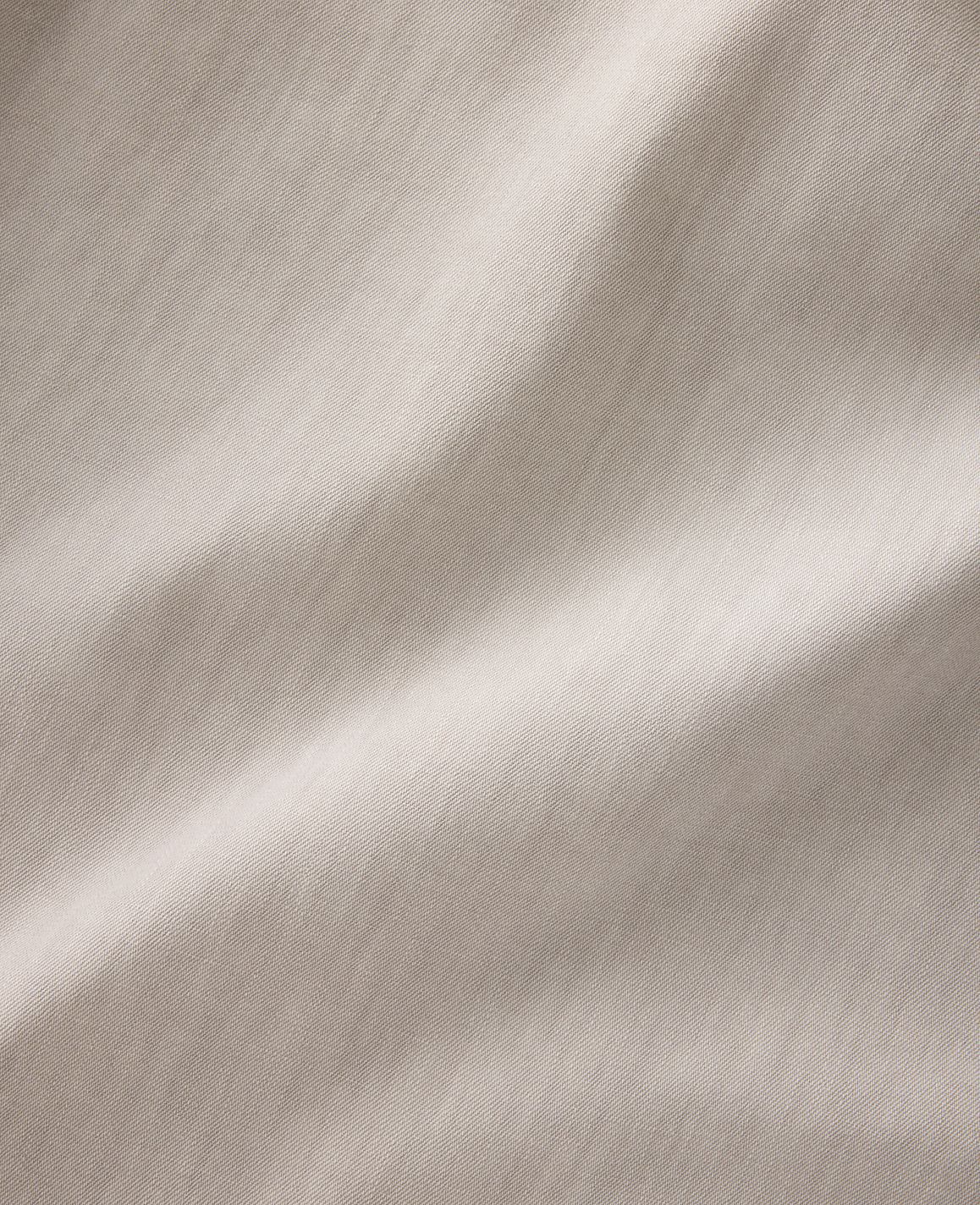 Soft, flowing folds of light brown fabric are illuminated by gentle light, creating subtle shadows and highlights across the textured surface.