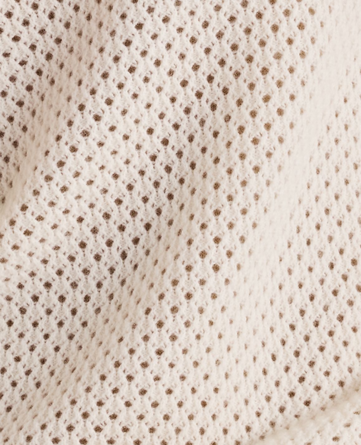 A close-up view of a cream-colored, loosely woven fabric with a textured, open-knit pattern fills the frame, revealing subtle shadows and folds in the material.
