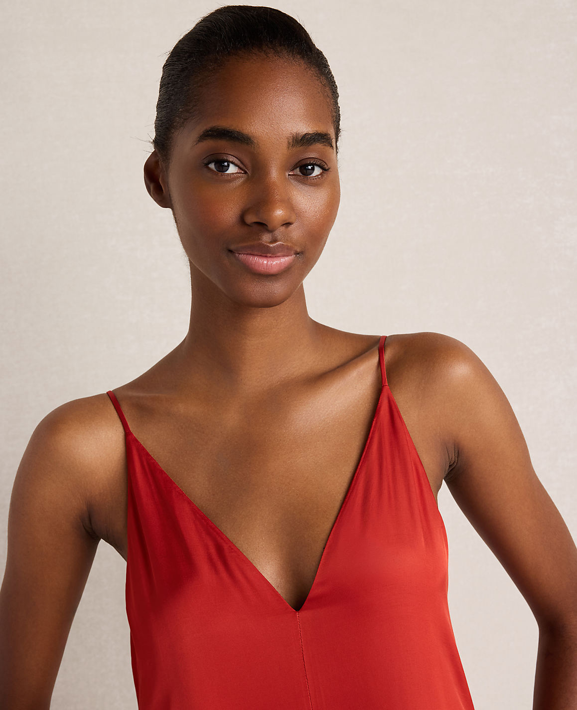 A young Black woman with dark hair pulled back wears a red V-neck dress against a plain, light-colored background.