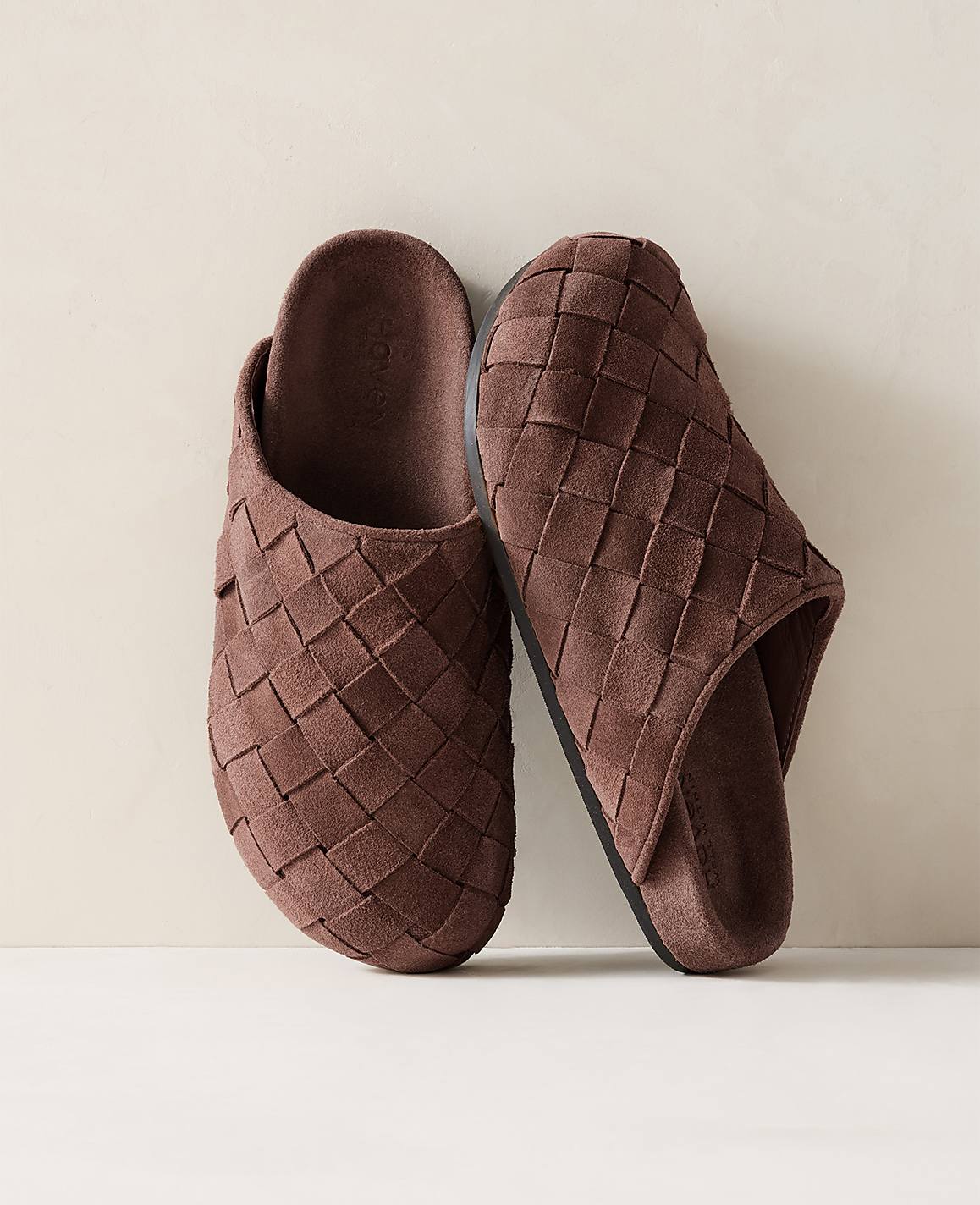 A pair of brown woven slippers rests on a light-colored surface against a soft, neutral background.