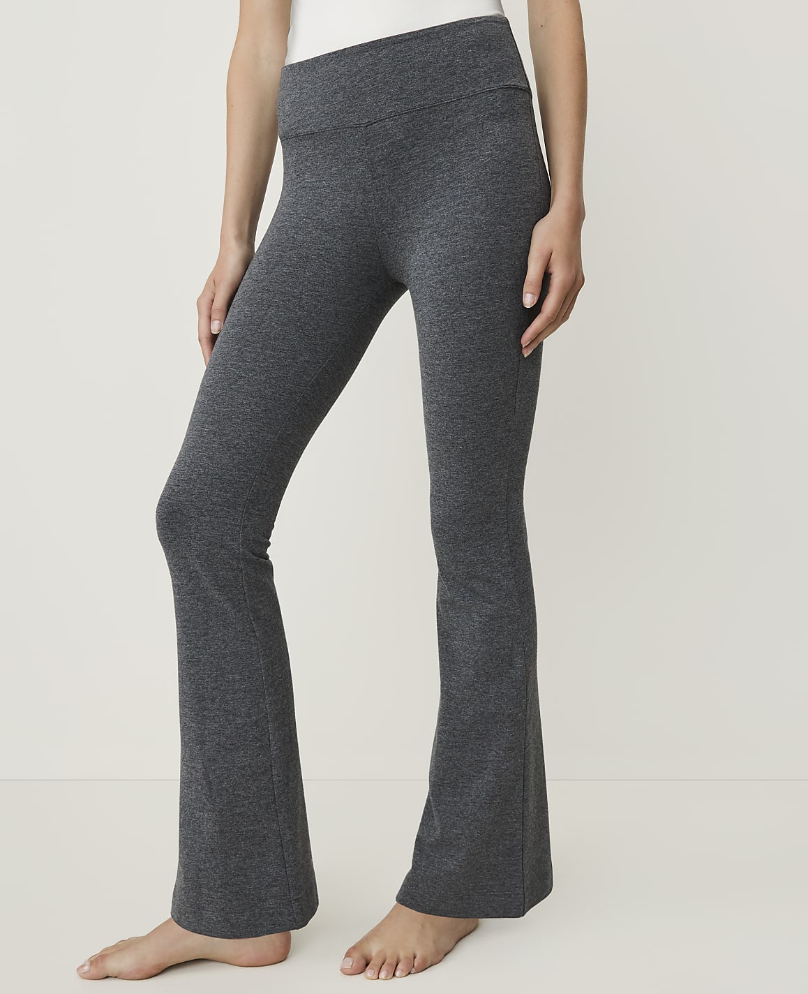 A person wearing charcoal grey flared yoga pants stands against a plain white background.