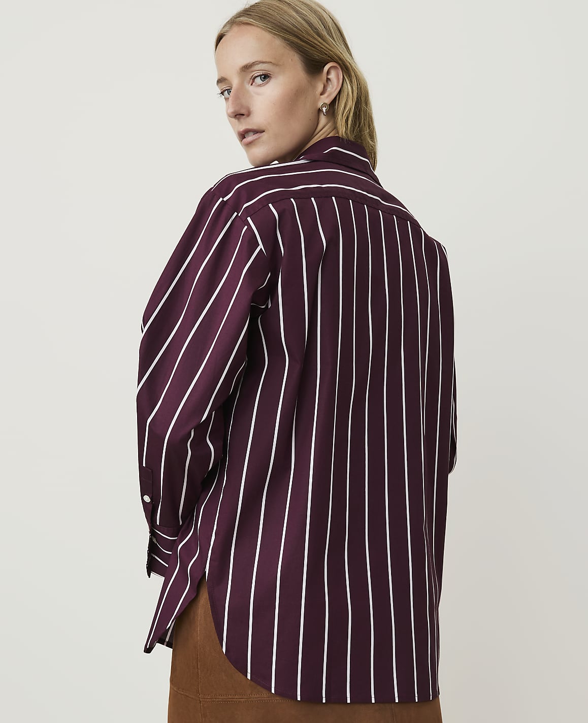 A woman in a burgundy and white striped shirt stands against a plain, light background.