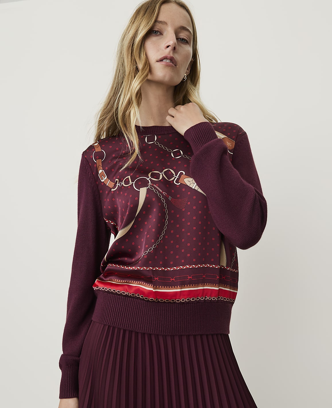 A woman in a burgundy sweater with a patterned front stands against a plain background.