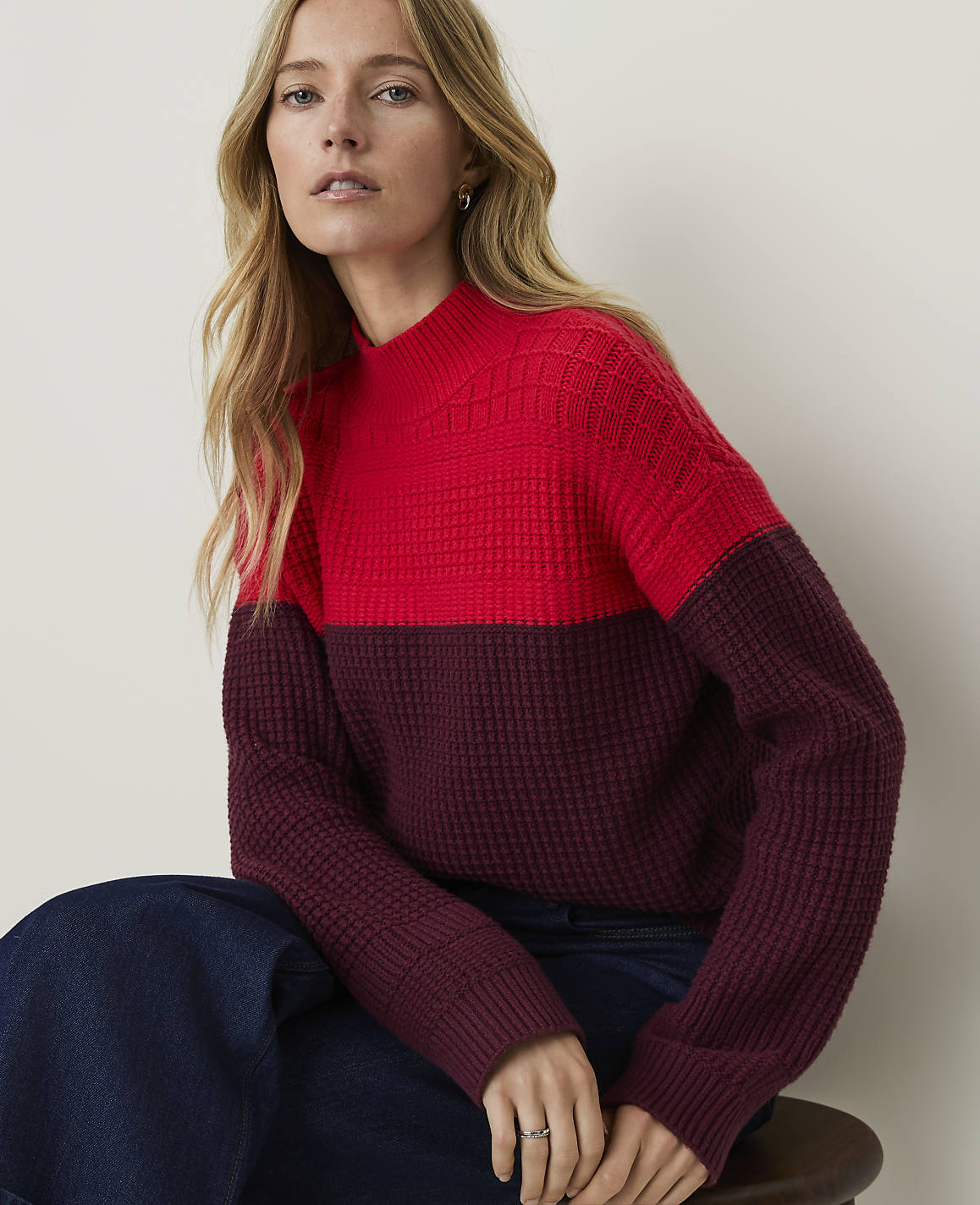 A woman in a two-toned red and burgundy sweater sits in front of a plain, light-colored background.