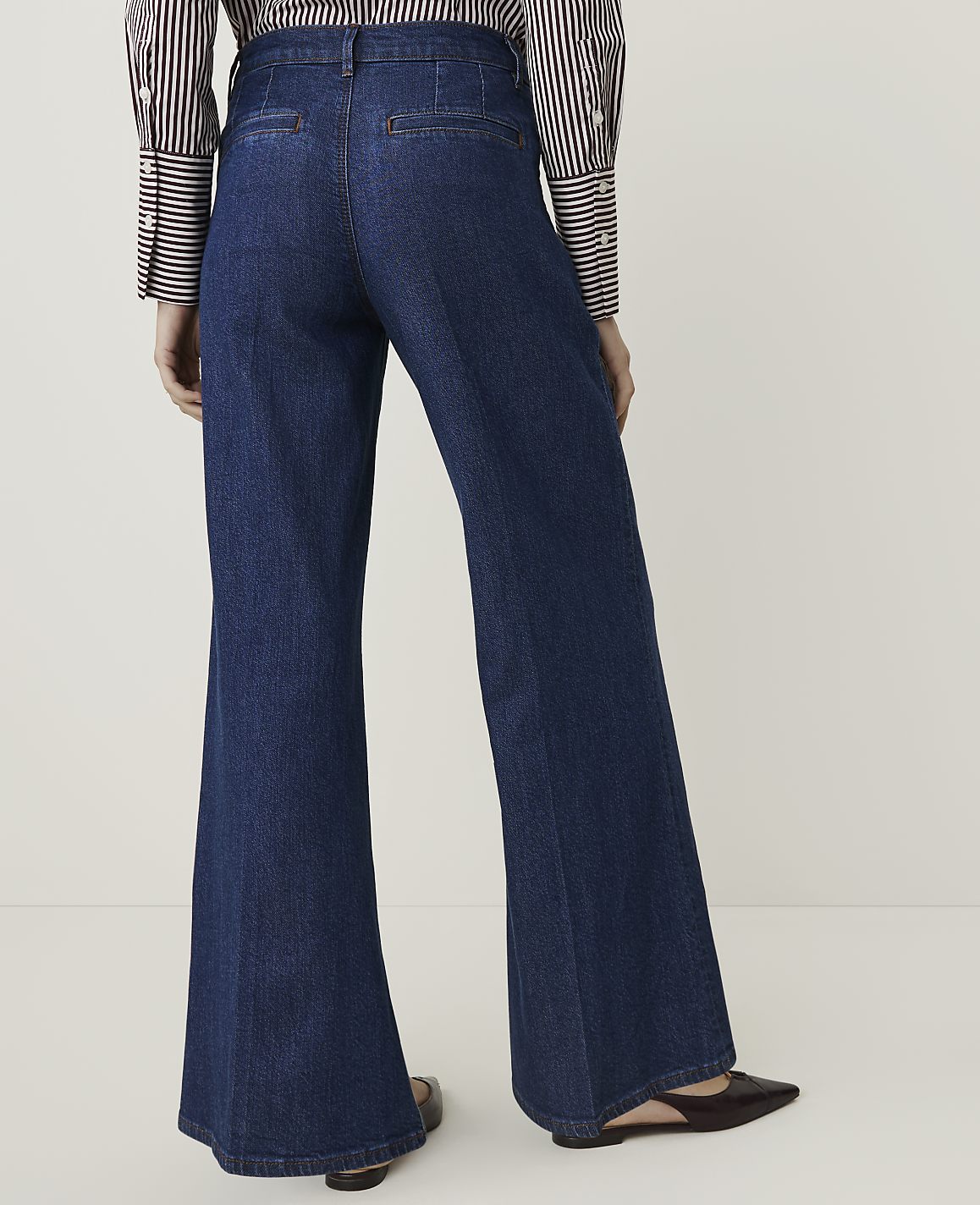 A person wearing dark wash flared jeans and a striped shirt stands against a plain white background.