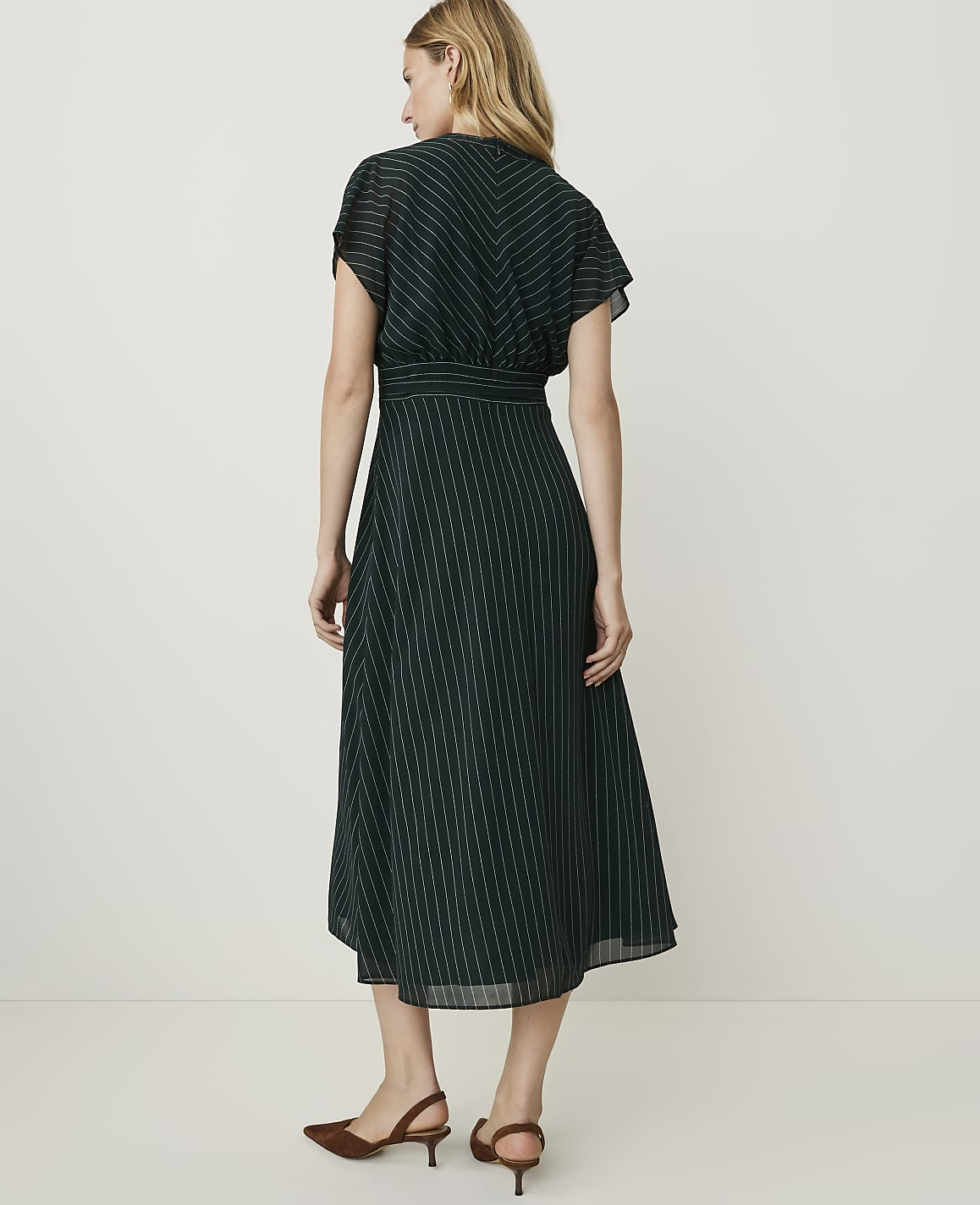 A woman in a dark green pinstripe dress stands against a plain, light-colored background.