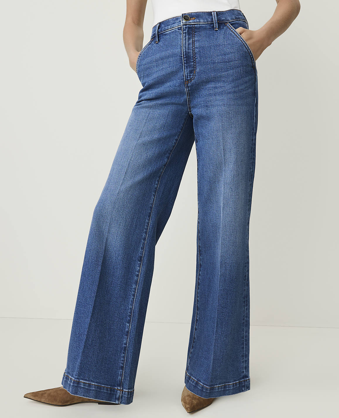 A person wearing wide-leg blue jeans and brown pointed-toe shoes stands against a plain white background.