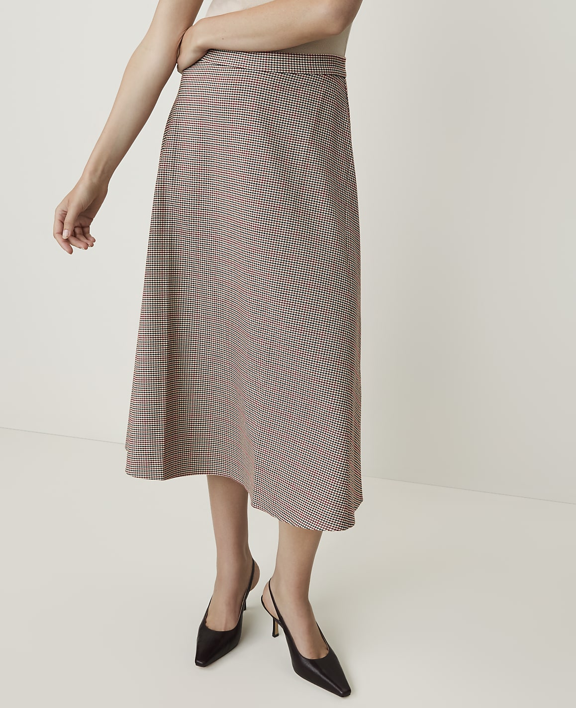 A woman models a plaid midi skirt and black slingback heels against a plain white background.