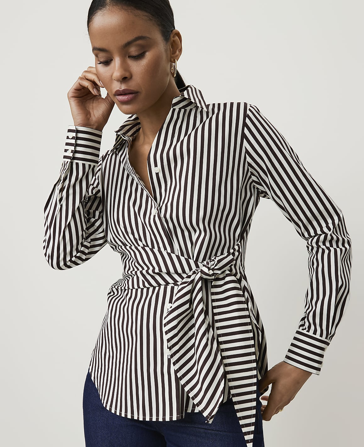 A woman in a black and white striped wrap shirt with a tie at the waist poses against a plain white background.