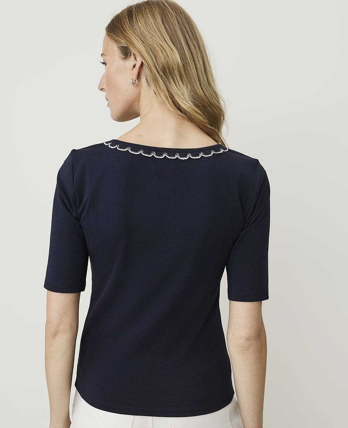 A woman in a navy blue top with a scalloped neckline stands against a plain white background.