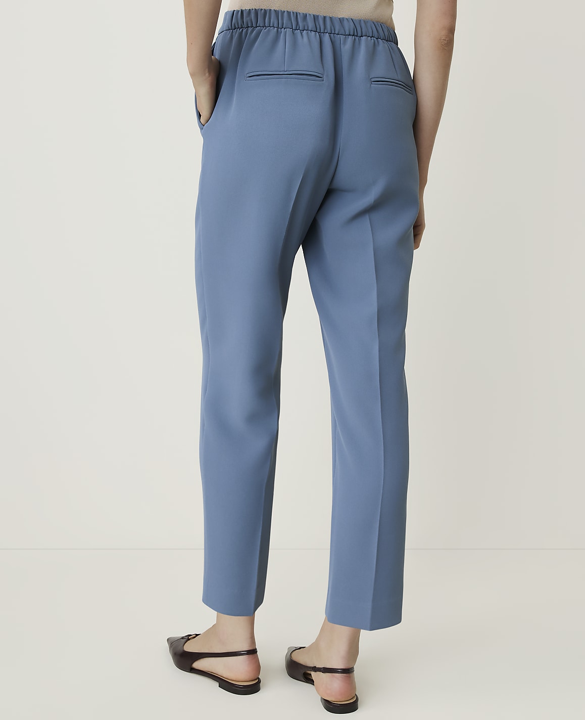 A person wearing blue trousers and black flats stands against a plain white background.