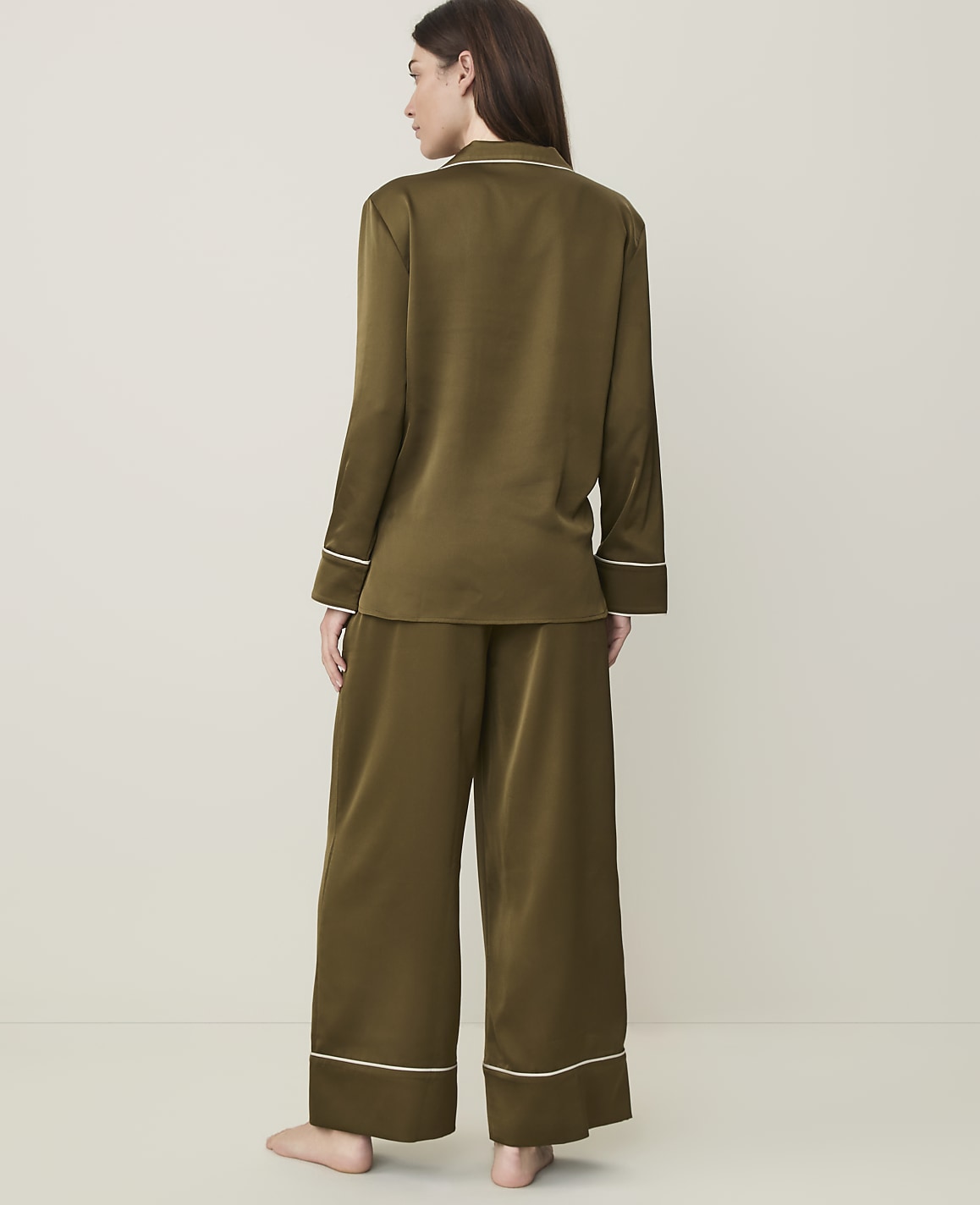 A woman in olive green satin pajamas stands against a plain, light-colored background.