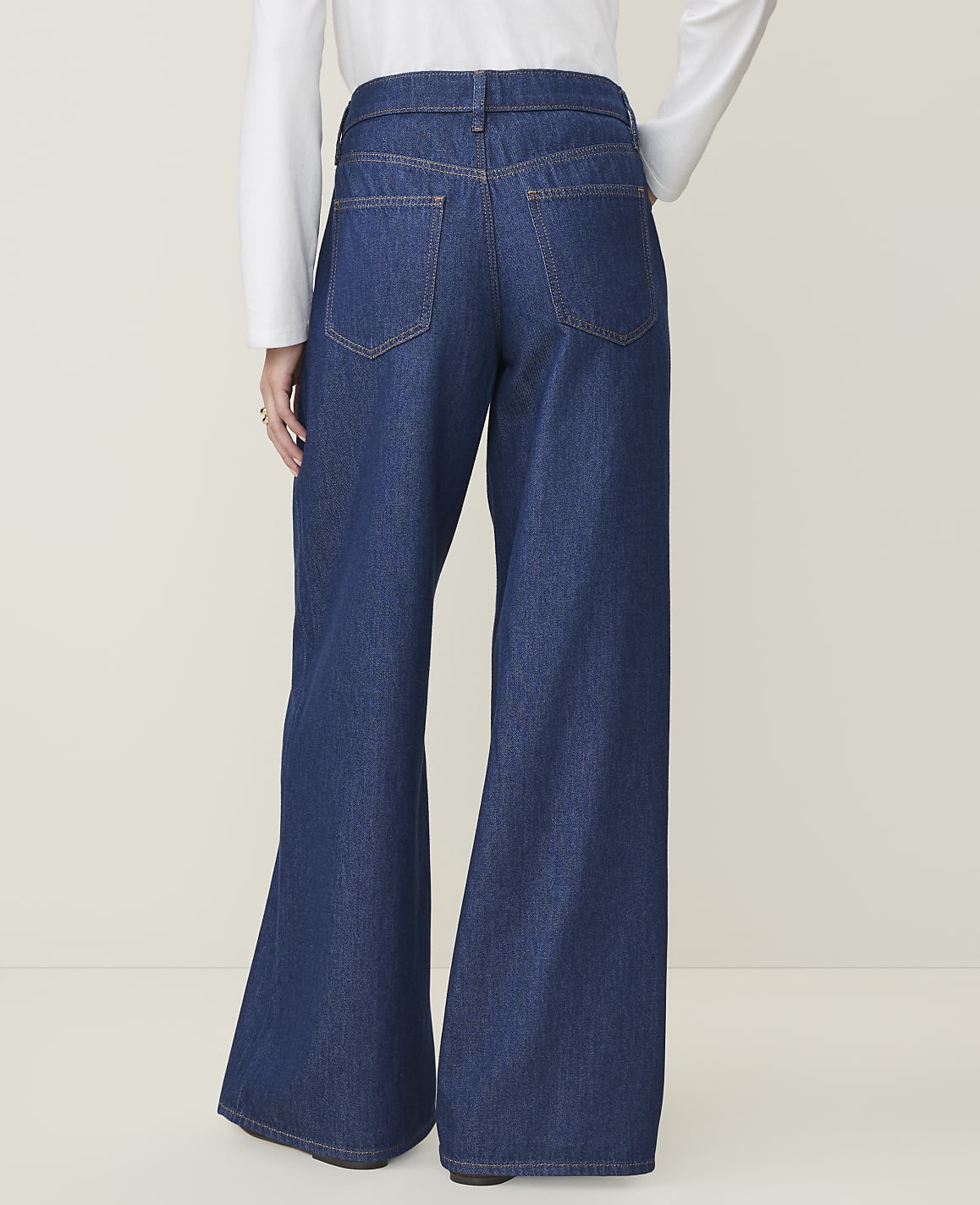 A person wearing dark wash wide-leg jeans stands against a plain, light-colored background.