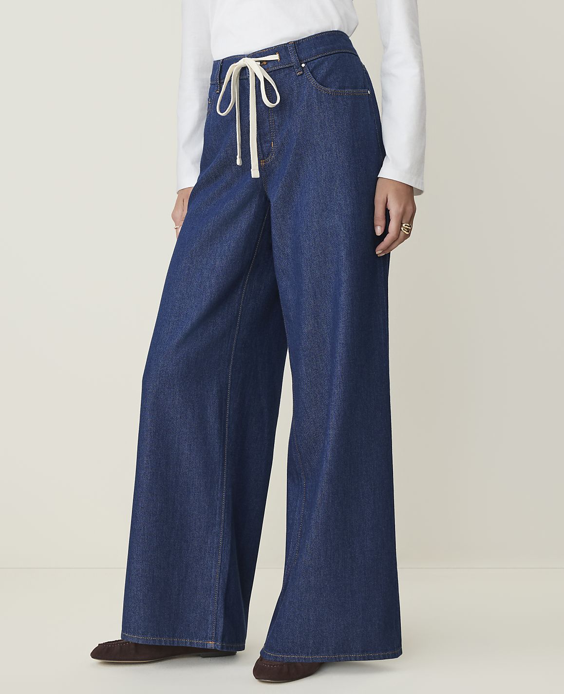 A person wearing wide-leg denim jeans with a white drawstring stands against a plain, light-colored background.