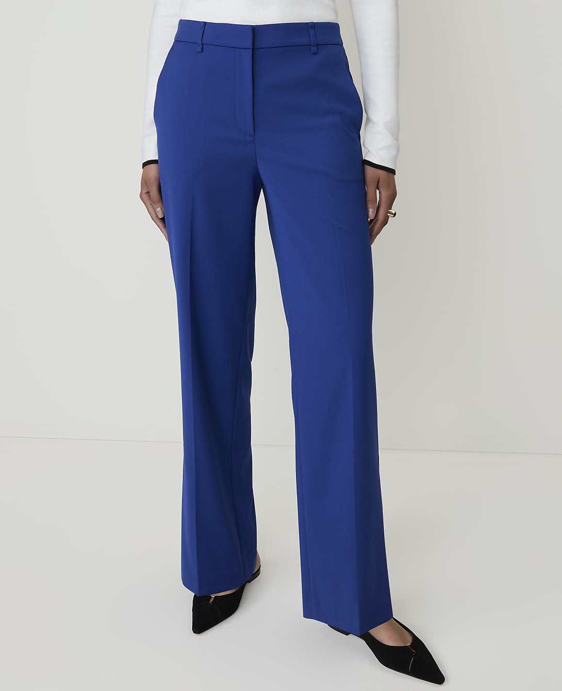 A person stands in bright blue wide-leg trousers and black pointed-toe shoes against a plain white background.