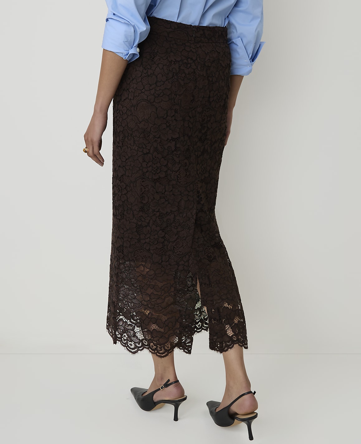 A person wearing a brown lace skirt and a blue shirt stands against a plain white background.