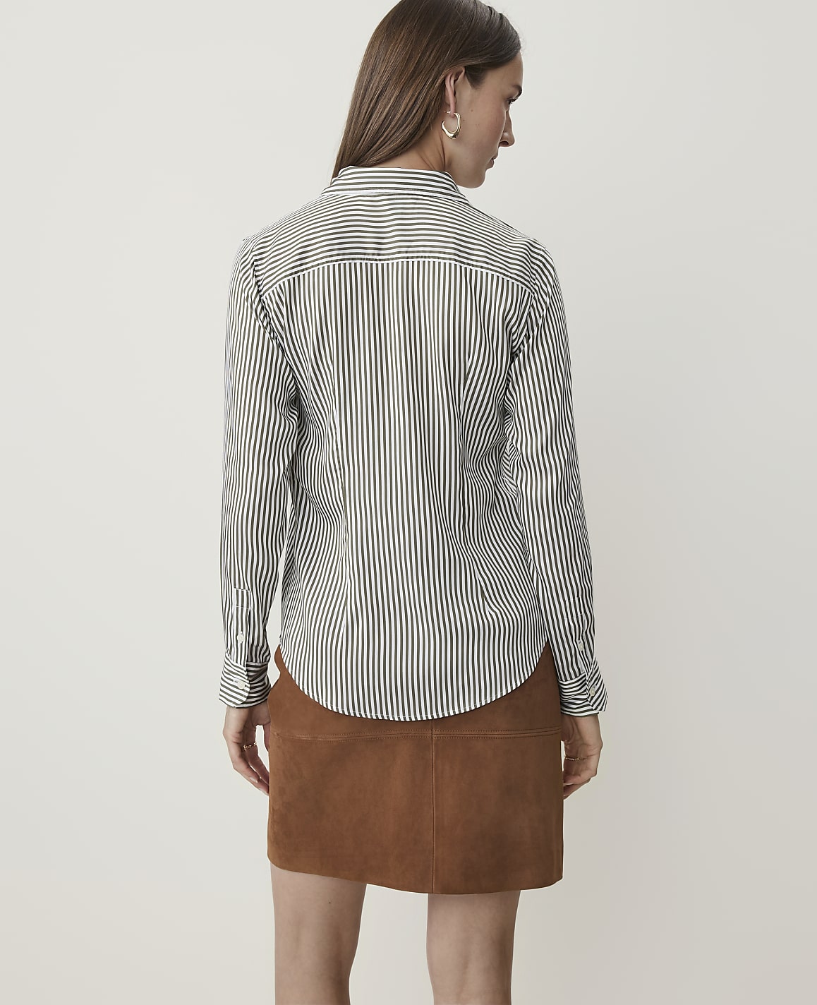 A woman in a striped shirt and brown skirt stands against a plain white background.