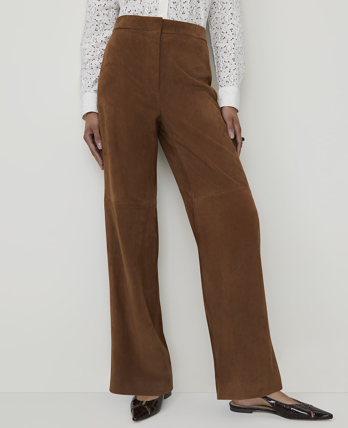 A person stands in brown corduroy pants and a white lace top against a plain white background.