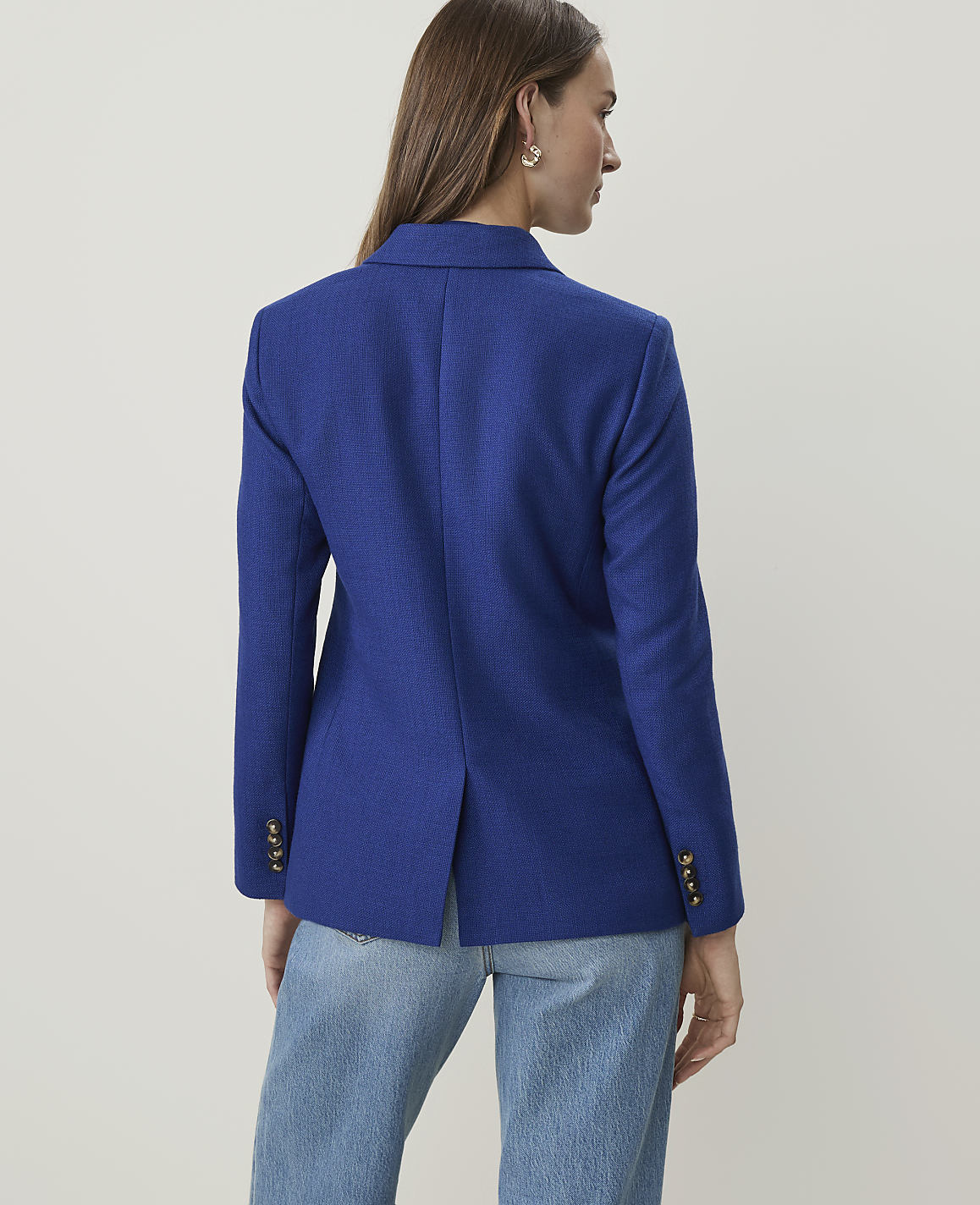 A woman in a blue blazer and jeans stands against a plain white background.