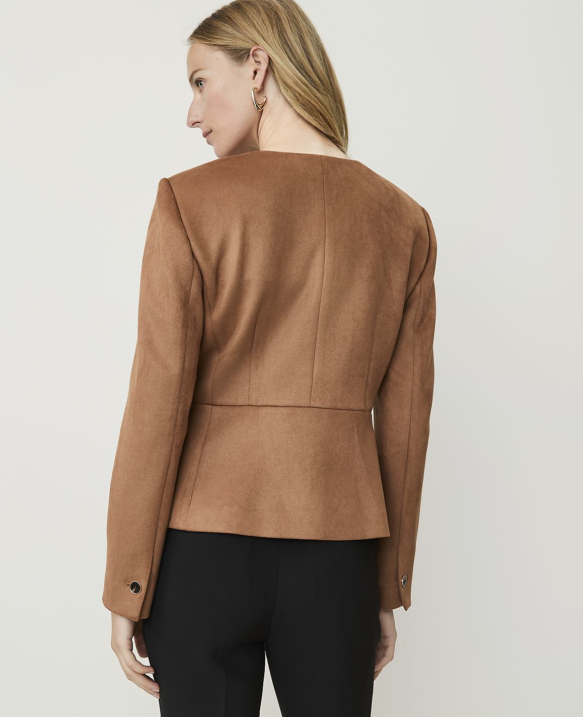 A woman in a brown jacket and black pants stands against a plain white background.