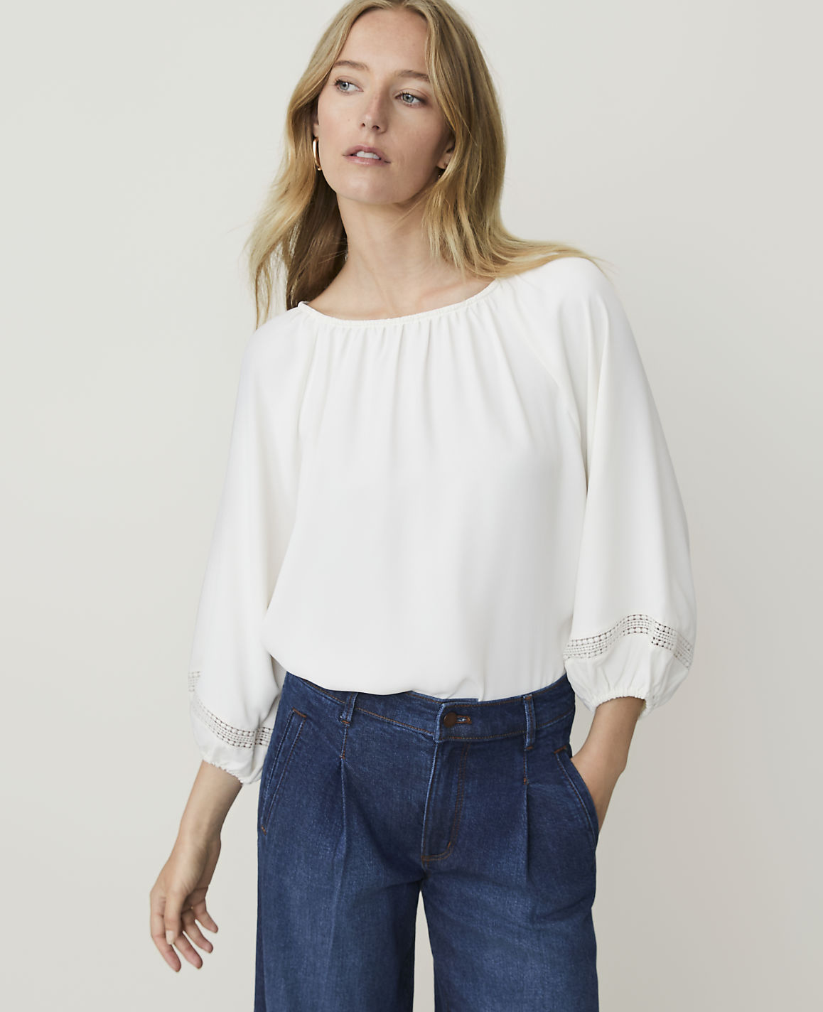 A woman in a white blouse and blue jeans stands against a plain white background.