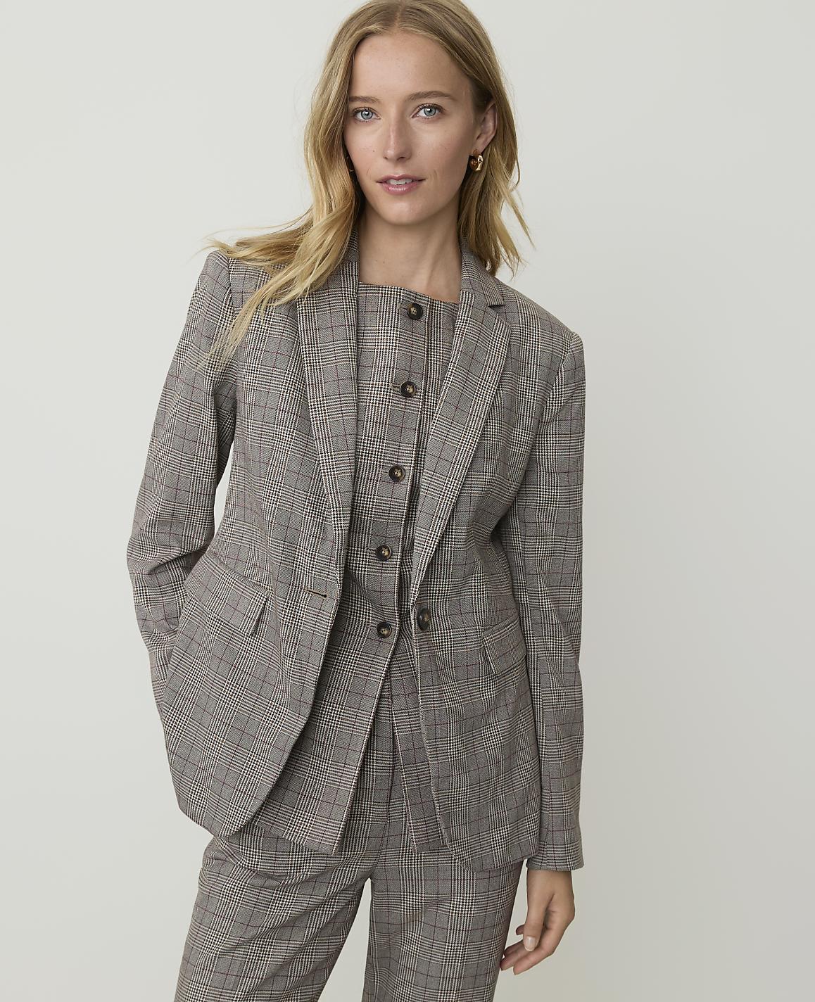 A woman in a plaid suit stands against a plain, light-colored background.