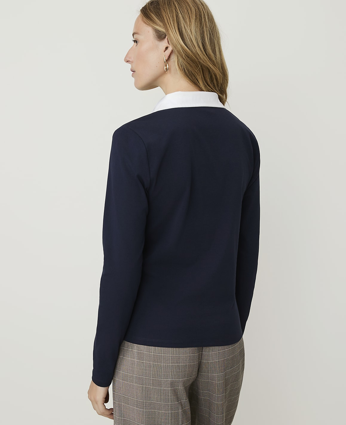 A woman in a navy sweater and plaid pants stands against a plain white background.