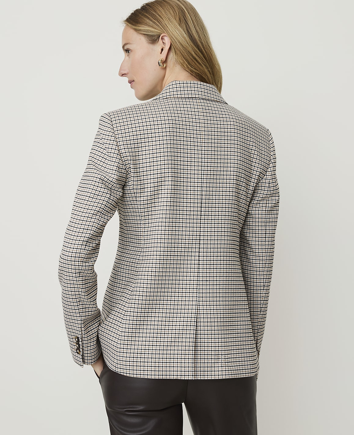 A woman in a checkered blazer stands against a plain, light background.
