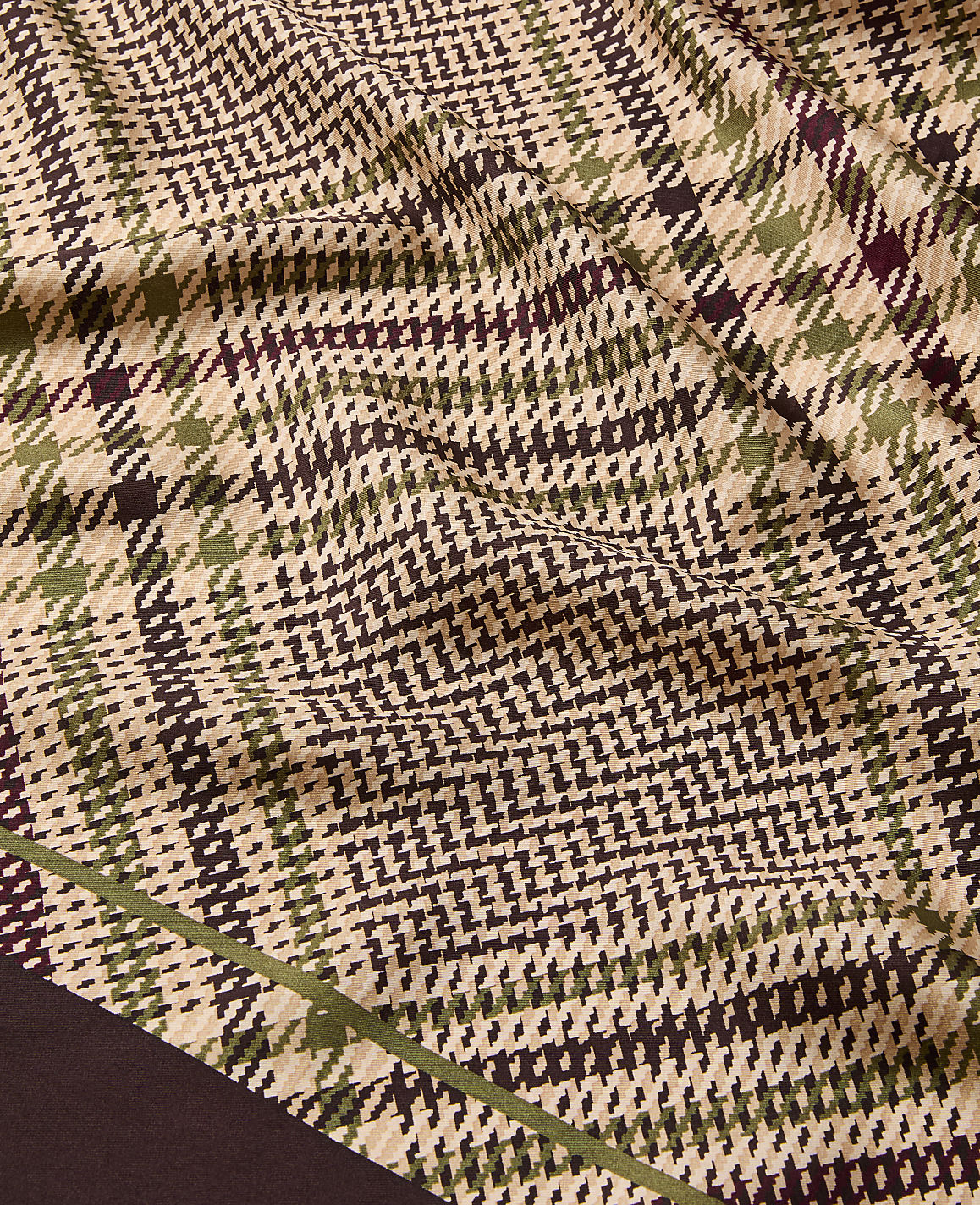 A close-up of a wrinkled fabric with a brown, green, and beige plaid pattern fills the foreground, while a dark brown border is visible at the bottom left.