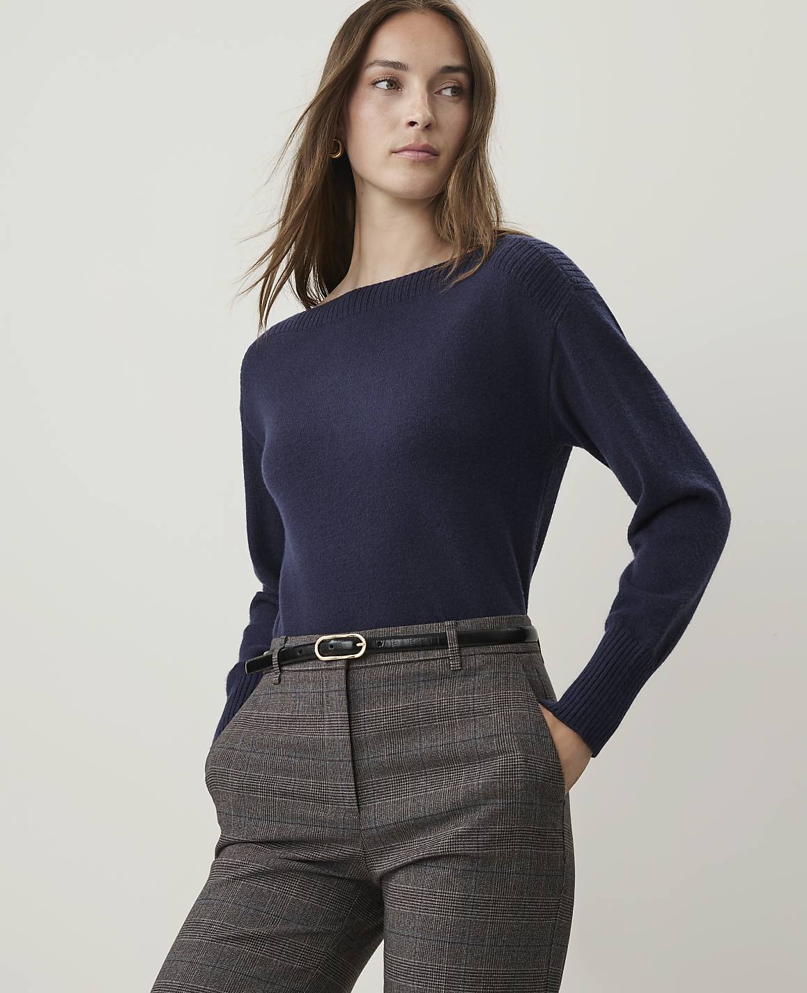 A woman in a navy sweater and plaid pants stands against a plain background.