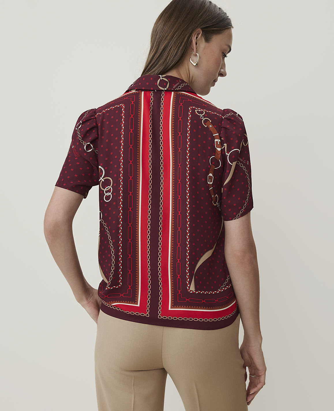A woman in a patterned maroon blouse stands against a plain, light-colored background.